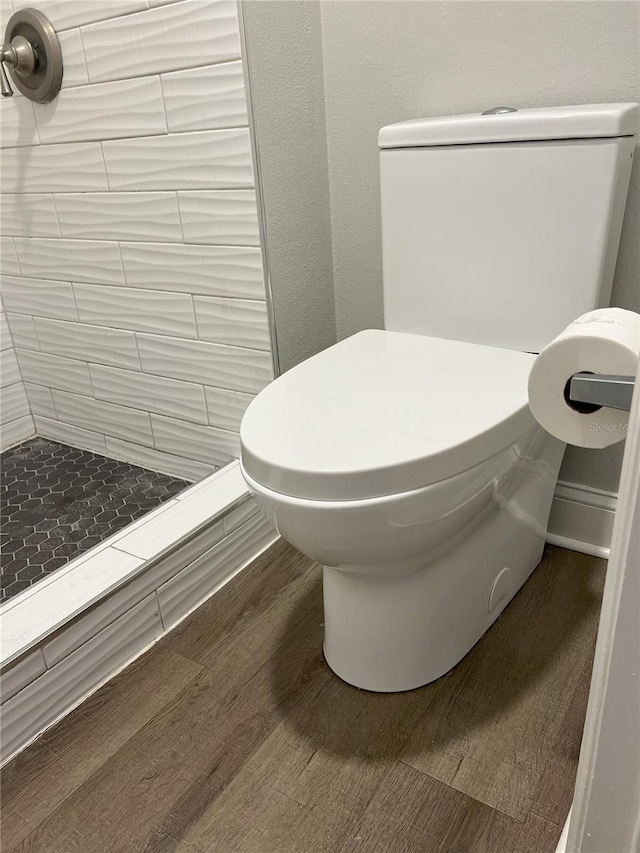 full bathroom with tiled shower, toilet, and wood finished floors