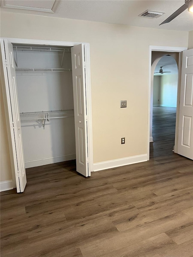 unfurnished bedroom featuring wood finished floors, arched walkways, a closet, baseboards, and visible vents