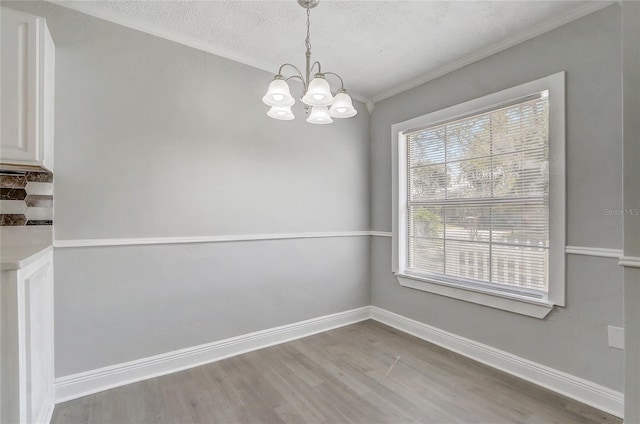 unfurnished dining area featuring ornamental molding, a textured ceiling, wood finished floors, a chandelier, and baseboards