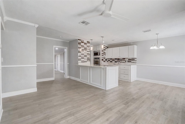 kitchen featuring tasteful backsplash, white cabinets, appliances with stainless steel finishes, light countertops, and ceiling fan with notable chandelier