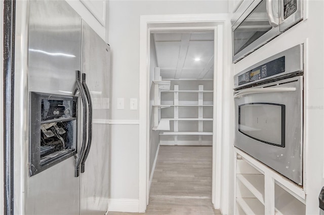 kitchen with light wood-style flooring, appliances with stainless steel finishes, white cabinets, and baseboards