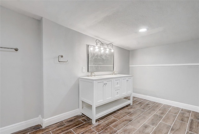 full bathroom featuring double vanity, baseboards, wood tiled floor, a textured ceiling, and a sink