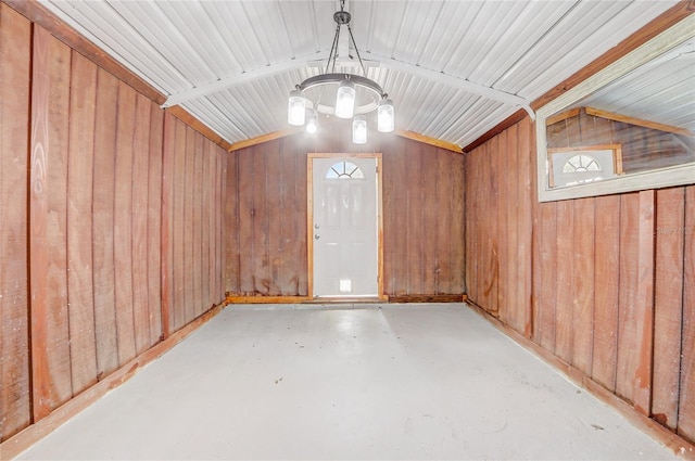 interior space featuring lofted ceiling, wooden walls, an inviting chandelier, and concrete flooring