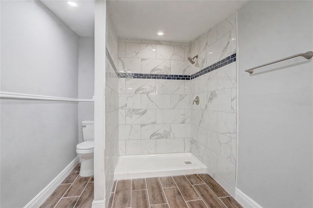 full bathroom with a tile shower, toilet, baseboards, and wood tiled floor