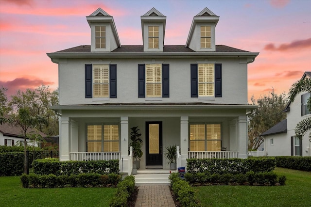 view of front facade featuring covered porch, stucco siding, and a front yard