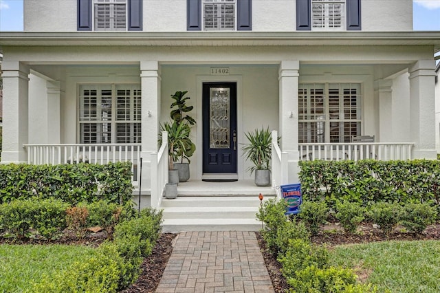 view of exterior entry featuring covered porch and stucco siding