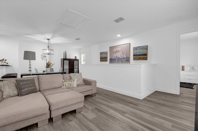 living area with light wood-type flooring, attic access, visible vents, and baseboards