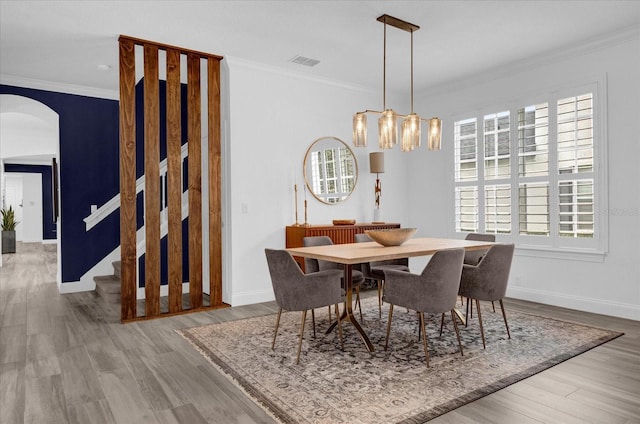 dining space with arched walkways, wood finished floors, visible vents, and crown molding