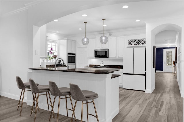 kitchen featuring arched walkways, stainless steel appliances, a peninsula, white cabinets, and dark countertops