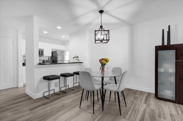 dining room featuring light wood finished floors, baseboards, a notable chandelier, and recessed lighting