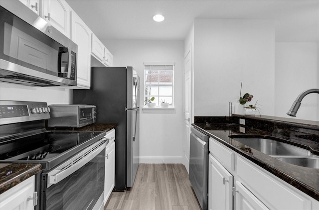 kitchen with a toaster, stainless steel appliances, a sink, white cabinets, and dark stone countertops