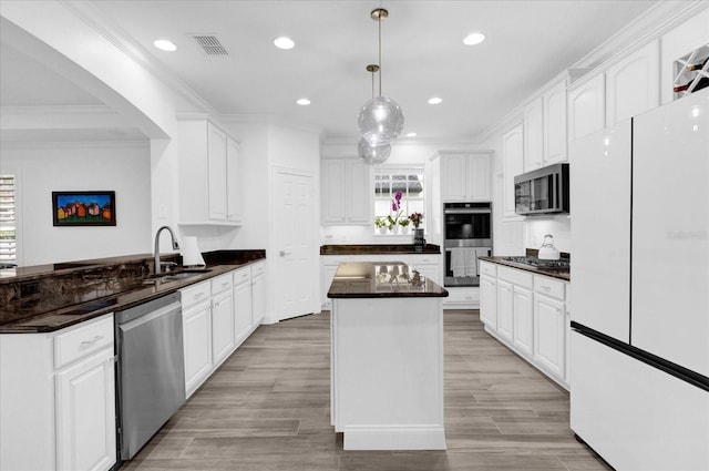 kitchen featuring white cabinets, dark countertops, a center island, stainless steel appliances, and a sink