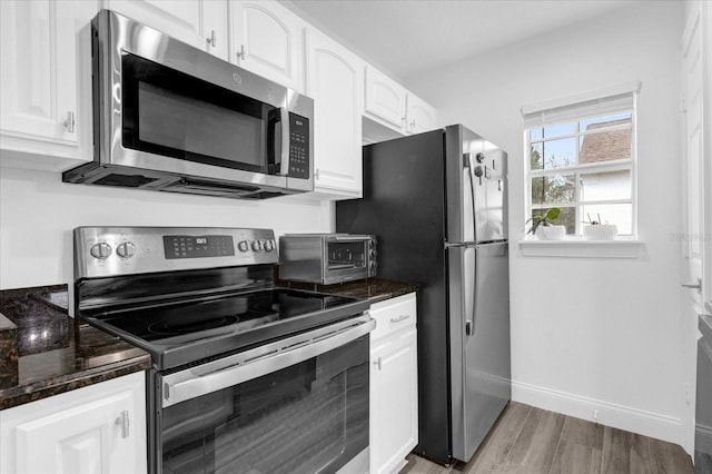 kitchen featuring a toaster, light wood finished floors, stainless steel appliances, white cabinets, and baseboards