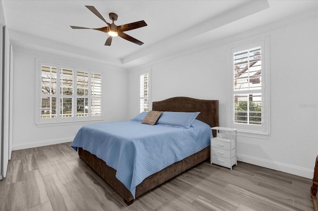 bedroom featuring baseboards, a tray ceiling, ceiling fan, and wood finished floors