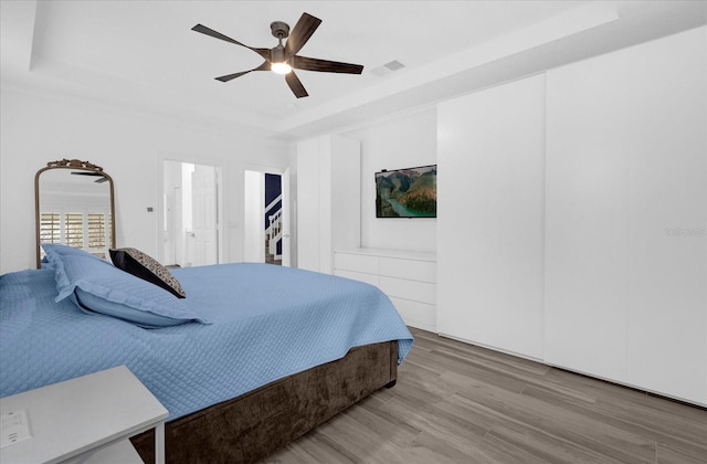 bedroom featuring a raised ceiling, visible vents, ceiling fan, and wood finished floors