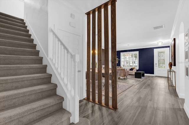 staircase with ornamental molding, visible vents, baseboards, and wood finished floors