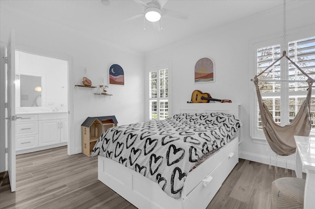 bedroom featuring light wood finished floors, ensuite bath, baseboards, and ornamental molding