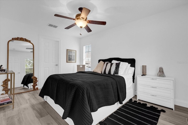 bedroom with ceiling fan, multiple windows, wood finished floors, and visible vents