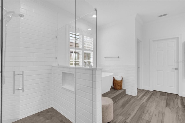 bathroom featuring visible vents, ornamental molding, wood finished floors, a shower stall, and tile walls