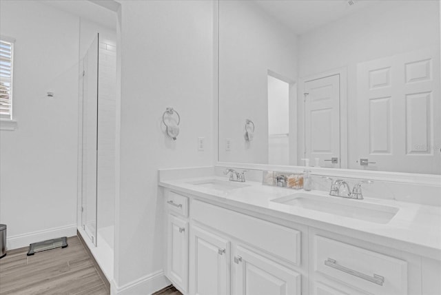 full bath featuring double vanity, a shower stall, a sink, and wood finished floors