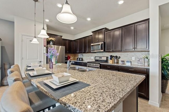 kitchen featuring dark brown cabinetry, decorative light fixtures, a kitchen island with sink, stainless steel appliances, and backsplash