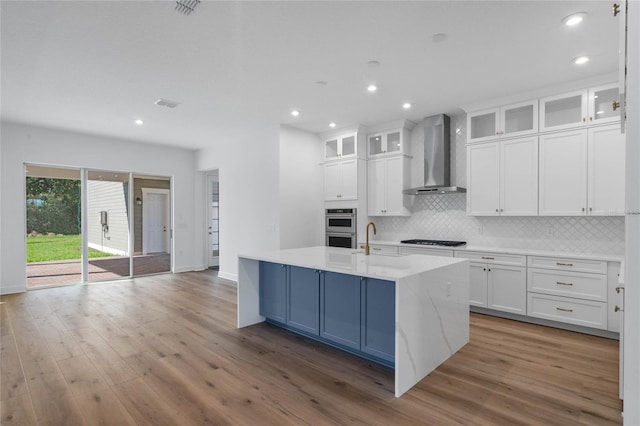 kitchen featuring stainless steel double oven, white cabinetry, stovetop, and wall chimney range hood