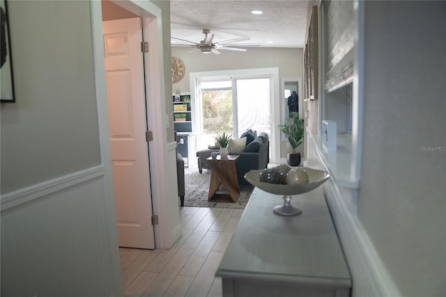 hallway featuring a textured ceiling, wainscoting, light wood-style flooring, and recessed lighting