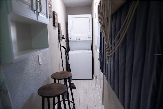 clothes washing area with stacked washer and dryer, a textured wall, and light wood finished floors