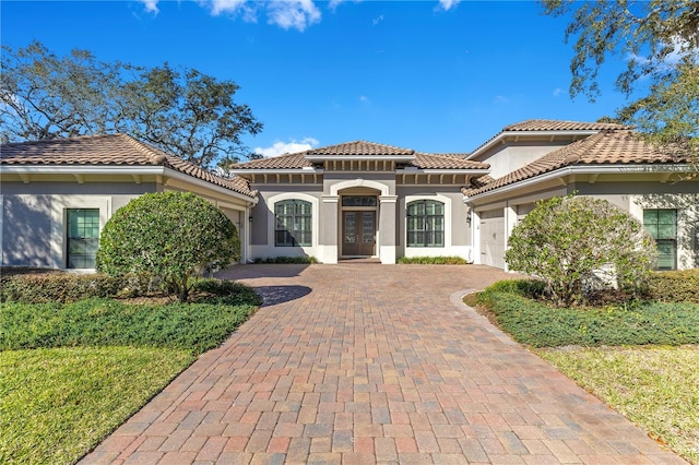 mediterranean / spanish home with a garage, french doors, decorative driveway, and stucco siding