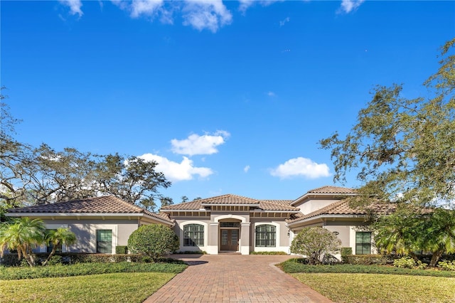 mediterranean / spanish house featuring a tile roof, french doors, decorative driveway, stucco siding, and a front yard