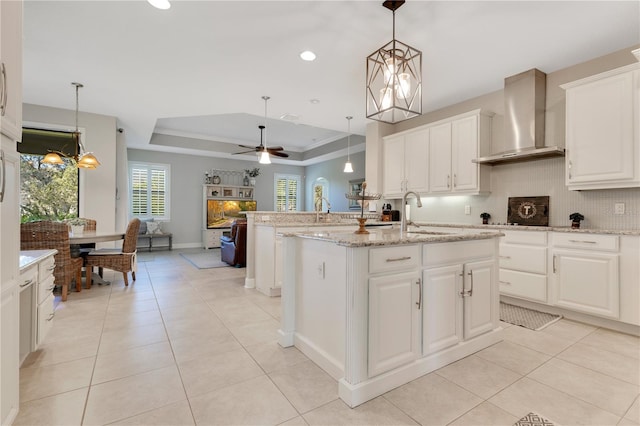 kitchen featuring light tile patterned floors, a sink, decorative backsplash, wall chimney exhaust hood, and a tray ceiling