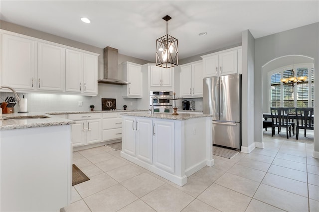 kitchen with arched walkways, appliances with stainless steel finishes, light tile patterned flooring, a sink, and wall chimney exhaust hood