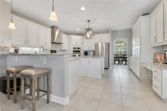 kitchen with arched walkways, a peninsula, white cabinetry, appliances with stainless steel finishes, and wall chimney exhaust hood