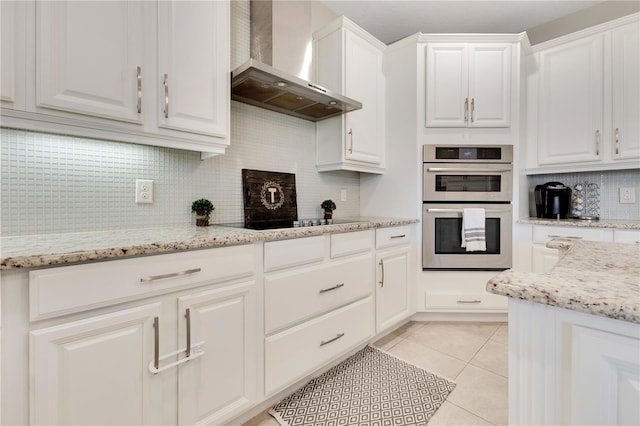 kitchen with wall chimney range hood, double oven, light tile patterned floors, and white cabinetry