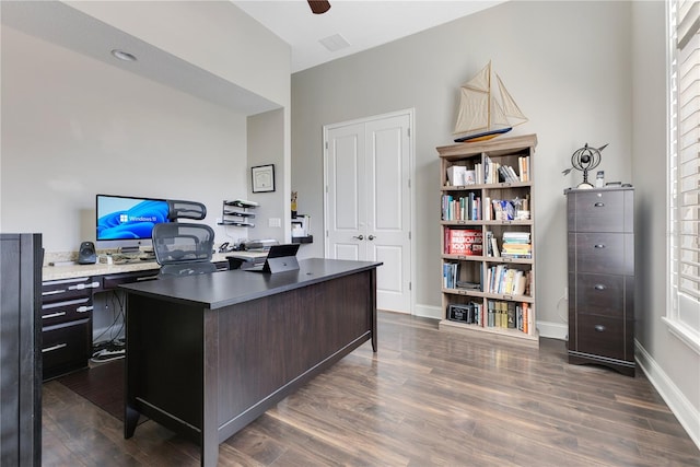 office featuring dark wood-type flooring, visible vents, baseboards, and a ceiling fan