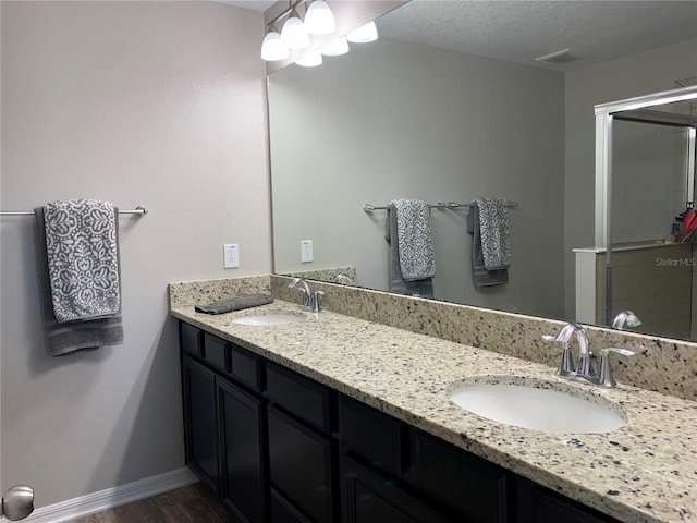 bathroom featuring a textured ceiling, double vanity, baseboards, and a sink