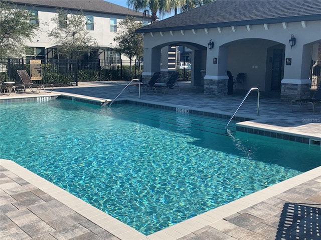 community pool with an outdoor structure, a storage structure, a patio area, and fence