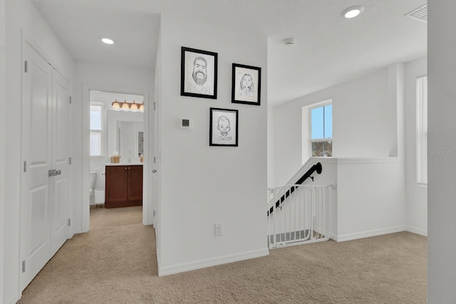 hallway featuring carpet floors, recessed lighting, baseboards, and an upstairs landing