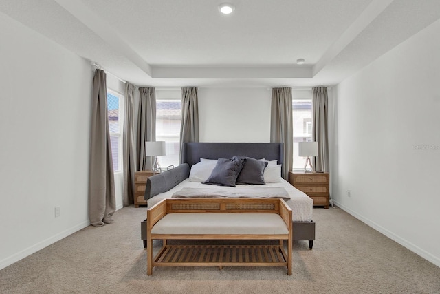 bedroom with a tray ceiling, light colored carpet, and baseboards