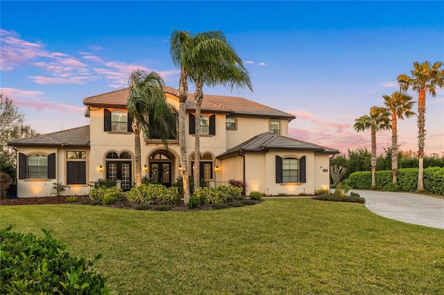 view of front of house featuring concrete driveway, a tiled roof, french doors, a front lawn, and stucco siding