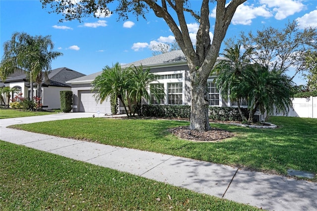 obstructed view of property with an attached garage, driveway, a front yard, and stucco siding