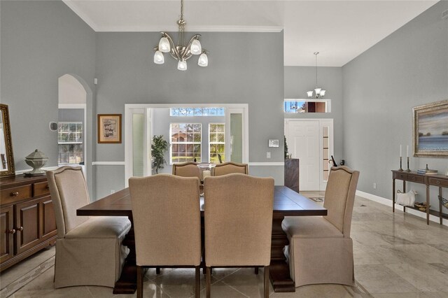 dining area featuring arched walkways, crown molding, a notable chandelier, a high ceiling, and baseboards