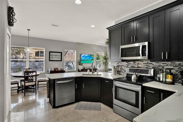 kitchen featuring stainless steel appliances, decorative backsplash, a sink, dark cabinetry, and a peninsula