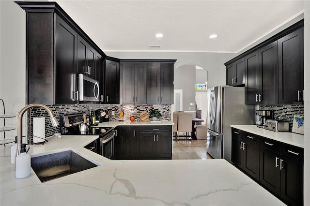 kitchen with arched walkways, appliances with stainless steel finishes, a sink, and dark cabinets