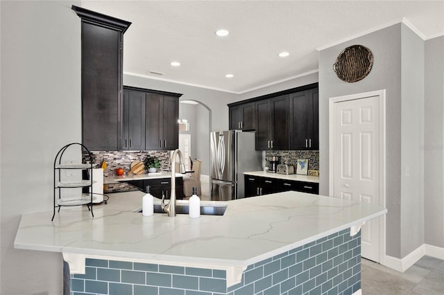 kitchen featuring arched walkways, light stone counters, a peninsula, a sink, and freestanding refrigerator