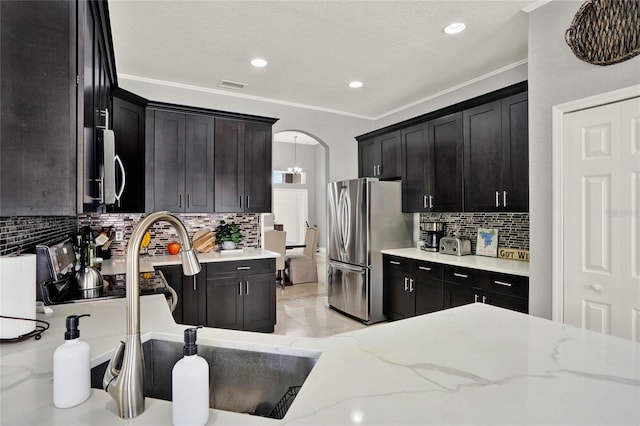 kitchen featuring arched walkways, visible vents, appliances with stainless steel finishes, light stone countertops, and crown molding