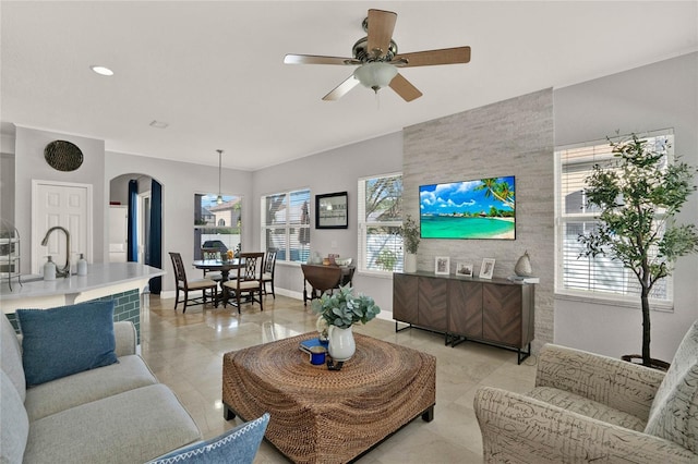 living area with arched walkways, a ceiling fan, and baseboards