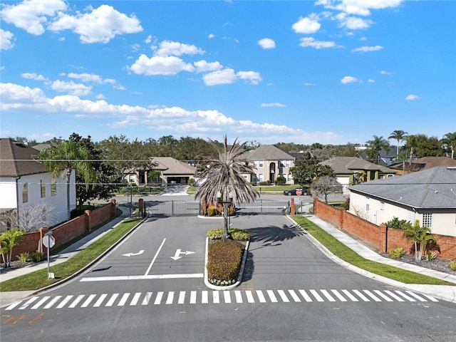 view of road with traffic signs, sidewalks, a gated entry, a residential view, and curbs