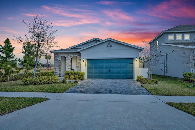 view of front of home with an attached garage, stone siding, decorative driveway, stucco siding, and a front lawn