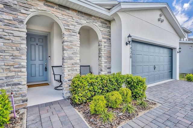 entrance to property with a garage, stone siding, driveway, and stucco siding